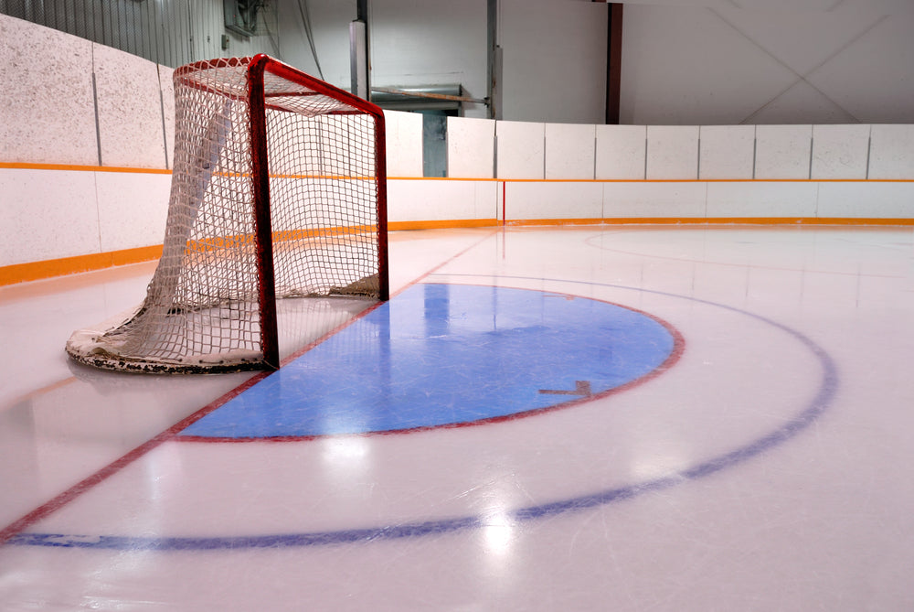 An indoor hockey rink with a goal net, ice surface, and white wall boards. Boards are made from HDPE Arena Boarp sheets.