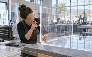 Woman fabricator measuring a clear acrylic aquarium panel before solvent cementing