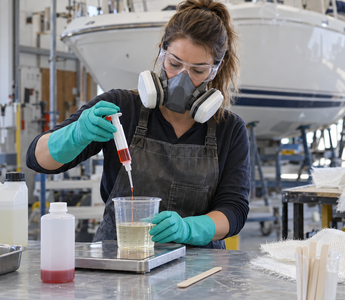 Female composites technician measuring MEKP catalyst into polyester resin in a clean boat repair workshop