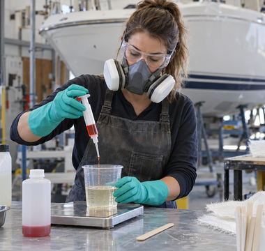 Female composites technician measuring MEKP catalyst into polyester resin in a clean boat repair workshop