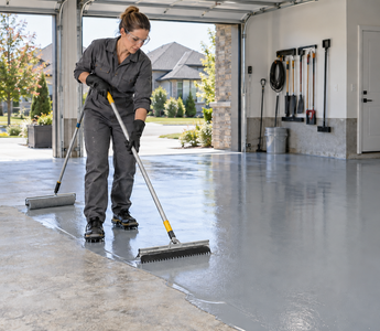 Woman applying grey epoxy floor coating with a squeegee and roller in a prepared garage