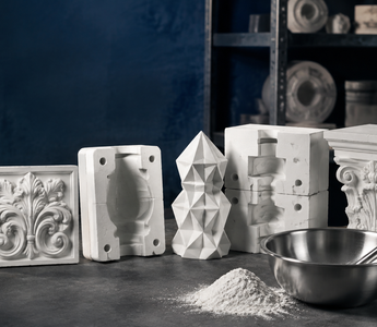 Premium casting studio with plaster reliefs, multi-part moulds, architectural ornament, a geometric gypsum casting, mixing bowl and white gypsum powder.