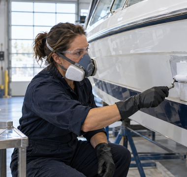 Woman marine technician applying white polyester gelcoat to a prepared fiberglass boat repair