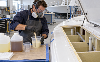 Marine technician mixing a controlled batch of two-part polyurethane foam beside a vented boat flotation cavity