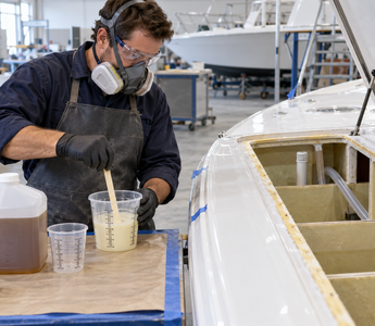 Marine technician mixing a controlled batch of two-part polyurethane foam beside a vented boat flotation cavity