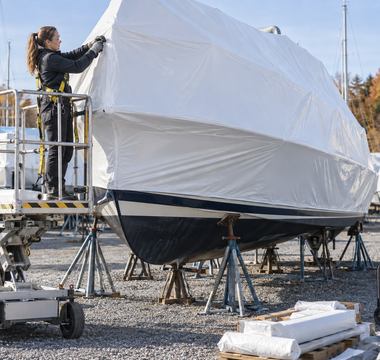 Woman shrink-wrapping a boat with marine film in a controlled outdoor work area
