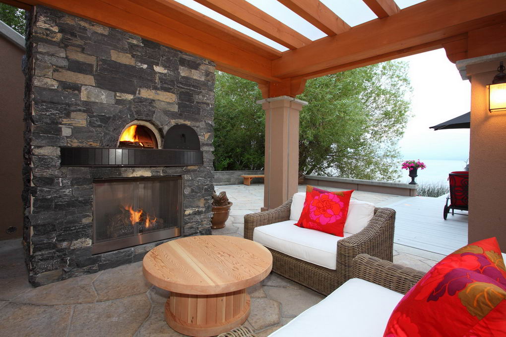 Stone fireplace and pizza oven beneath a clear polycarbonate patio roof