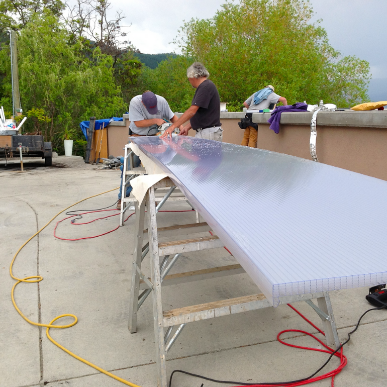 Contractors preparing a long clear multiwall polycarbonate roof panel