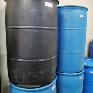 A black reconditioned 55 gallon plastic drum with visible signs of wear, stacked among other drums.